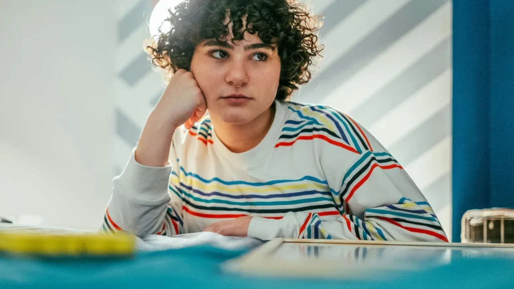 נערה יושבת ליד שולחן עם יד על הראש, מתוסכלת מול משימה